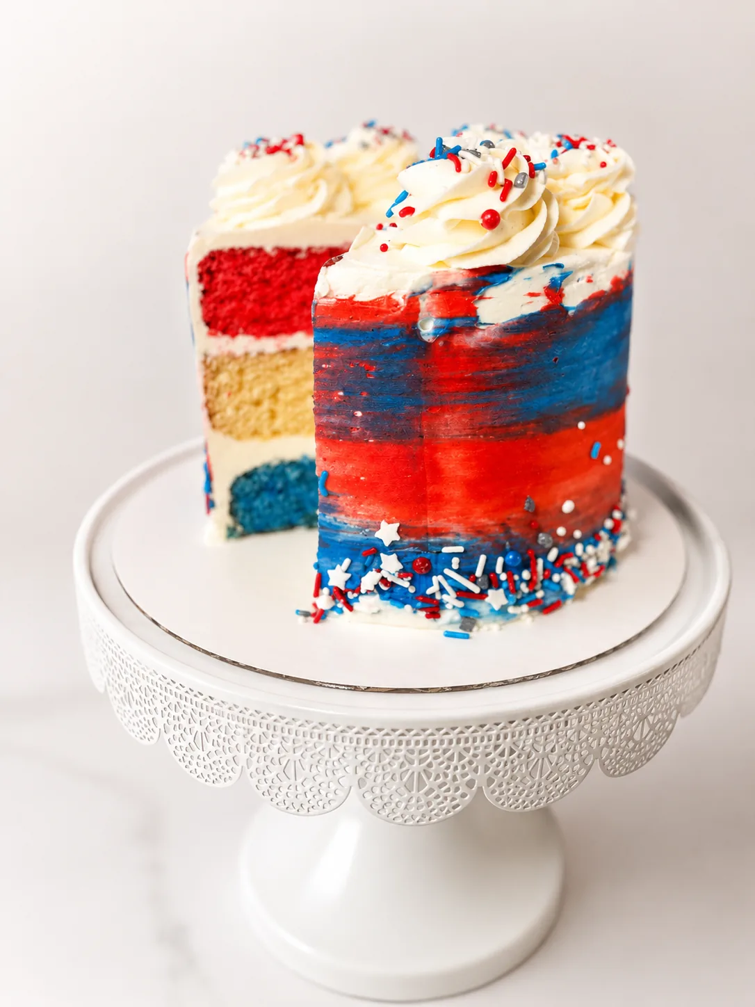 Sliced Bomb Pop Cake from Crumb Believable Bakery with cherry, vanilla, and blue raspberry cake layers, buttercream frosting, and patriotic sprinkles.